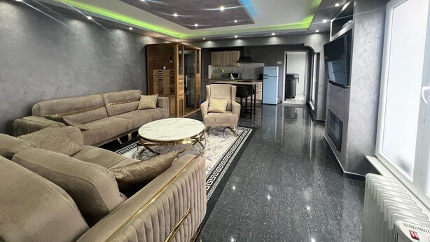 Sala de estar moderna com sofá modular, uma mesa de centro redonda e área de cozinha ao fundo.
