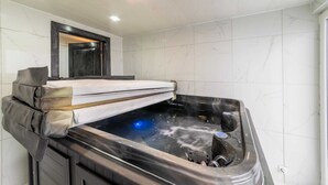 Um banheiro moderno com uma banheira de hidromassagem preta, um banco de madeira e um espelho sobre a banheira.