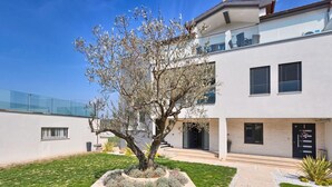 Un bâtiment moderne à deux étages, doté d’un jardin aménagé, d’un chemin pavé et surplombé d’un ciel bleu azur.