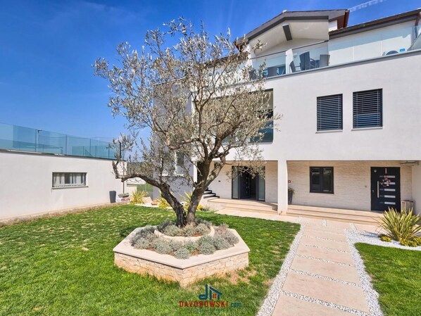 A modern two-story building with a landscaped garden, a paved pathway, and a clear blue sky. - met Wellness Studio D (Pula)