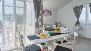 Une salle à manger lumineuse, avec une table dressée pour deux personnes, agrémentée d’un plateau de fruits et d’une théière verte.