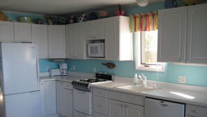 Una cocina con armarios blancos, estufa, refrigerador y microondas.
