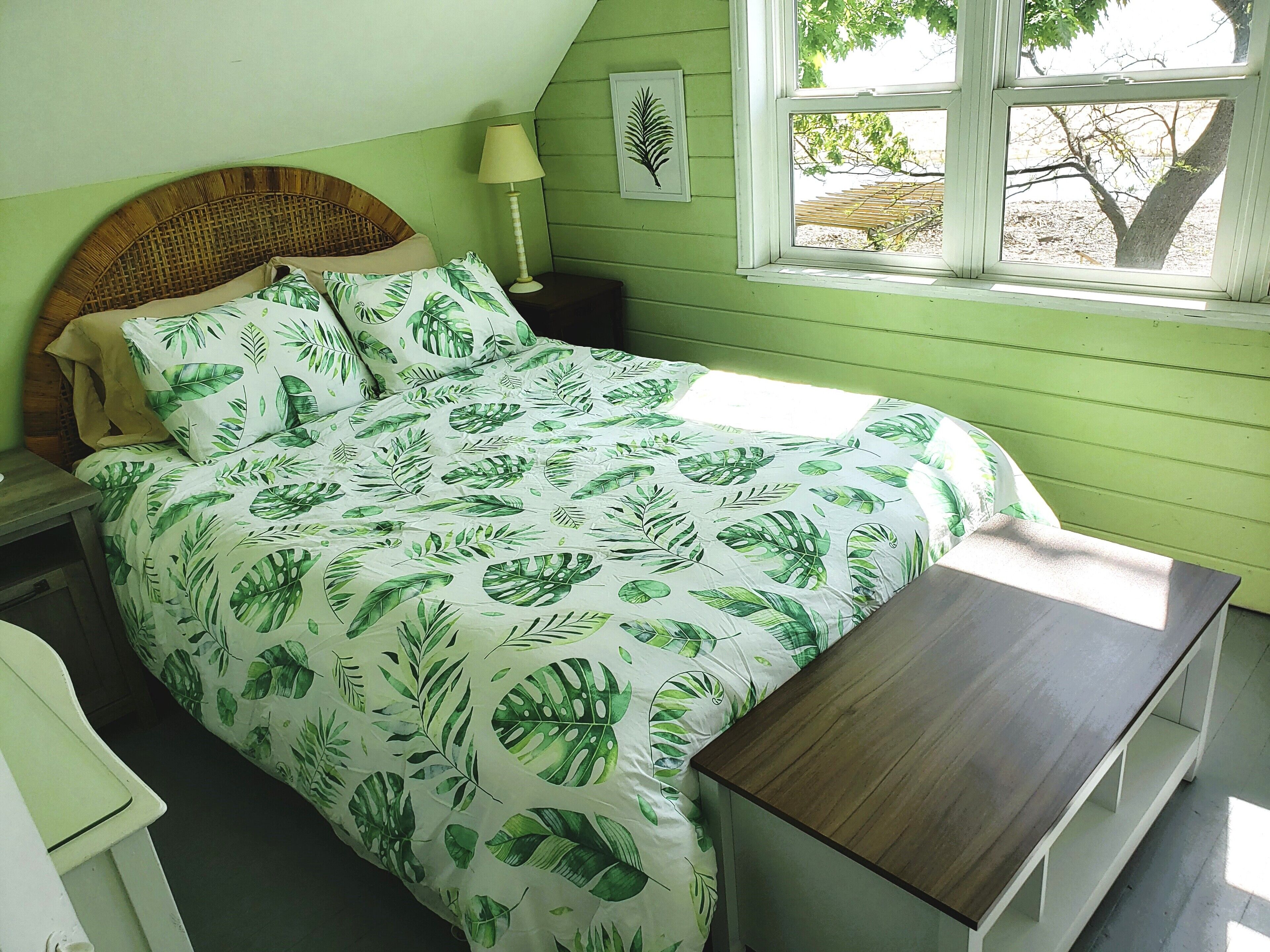 A bedroom with a bed, a nightstand, a bedside table, a window, and a view of trees.