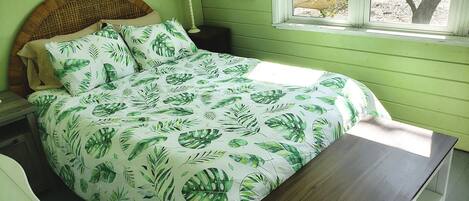 A bedroom with a bed, a nightstand, a bedside table, a window, and a view of trees.