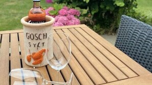 Uma mesa de madeira com uma garrafa de vinho Gosch Sylt e dois copos de vinho vazios.