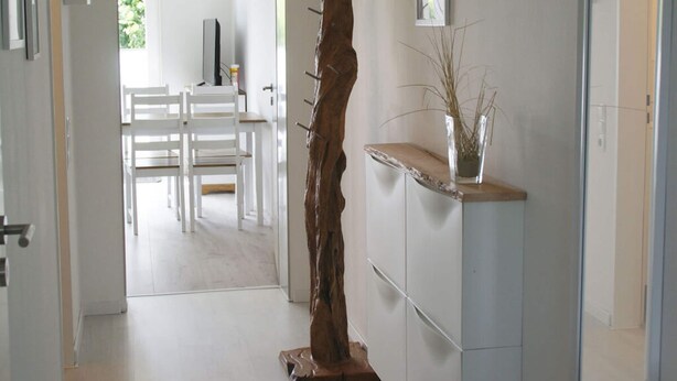 Um corredor com uma escultura de madeira, um armário branco e um espelho.
