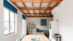 Ein modernes Wohnzimmer mit Holzboden, einem Esstisch mit Stühlen, einer Couch, einem Bücherregal und einem Kühlschrank.