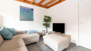 Ein modernes Wohnzimmer mit einer Couch, einem Hocker, einem Fernseher und einem Gemälde an der Wand.
