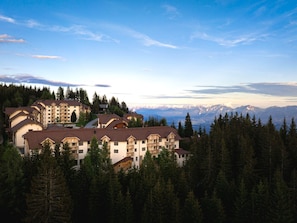 A mountain resort with multiple buildings surrounded by dense forest and a view of snow-capped mountains. - Holiday Apartment in Gerlitzen With Wellness Area (Treffen)