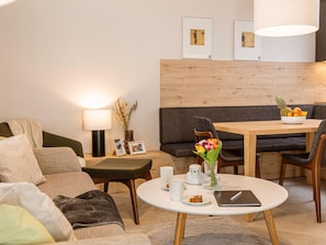 A modern living room with a sofa, a round table with a laptop, a vase with flowers, and a bowl of fruit. - Holiday Apartment in Gerlitzen With Wellness Area (Treffen)