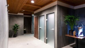 A modern hallway with a wooden ceiling, grey and dark grey walls, and a tiled floor. There are two doors, a potted plant, and a shelf with a Buddha statue and a decorative item. - Holiday Apartment in Gerlitzen With Wellness Area (Treffen)