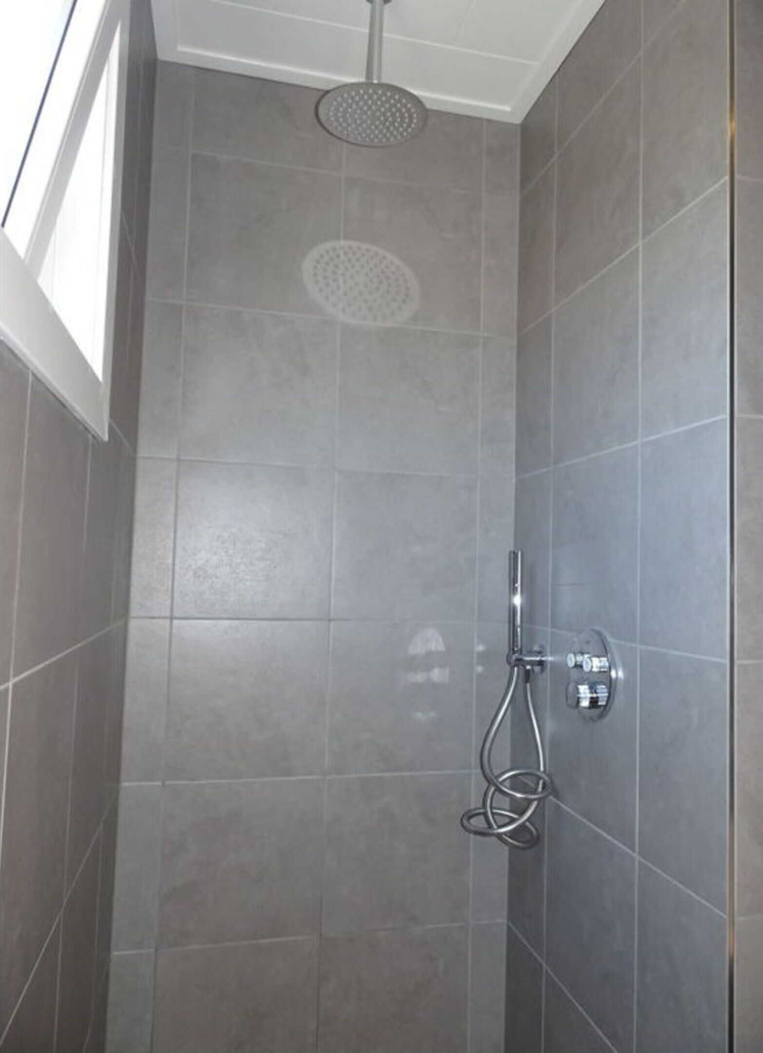Ducha con cabezal de ducha de mano y panel de control en la pared.