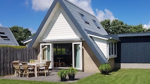 Una casa moderna con techo inclinado, un patio con muebles de exterior y un patio trasero cercado.