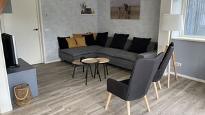 Una sala de estar moderna con un sofá seccional gris, un sillón negro y dos mesas redondas.