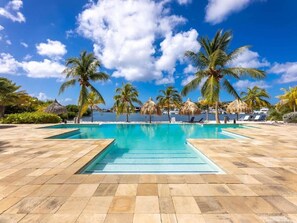 Ein Poolbereich mit klarem, blauem Wasser, Palmen und Blick aufs Meer.