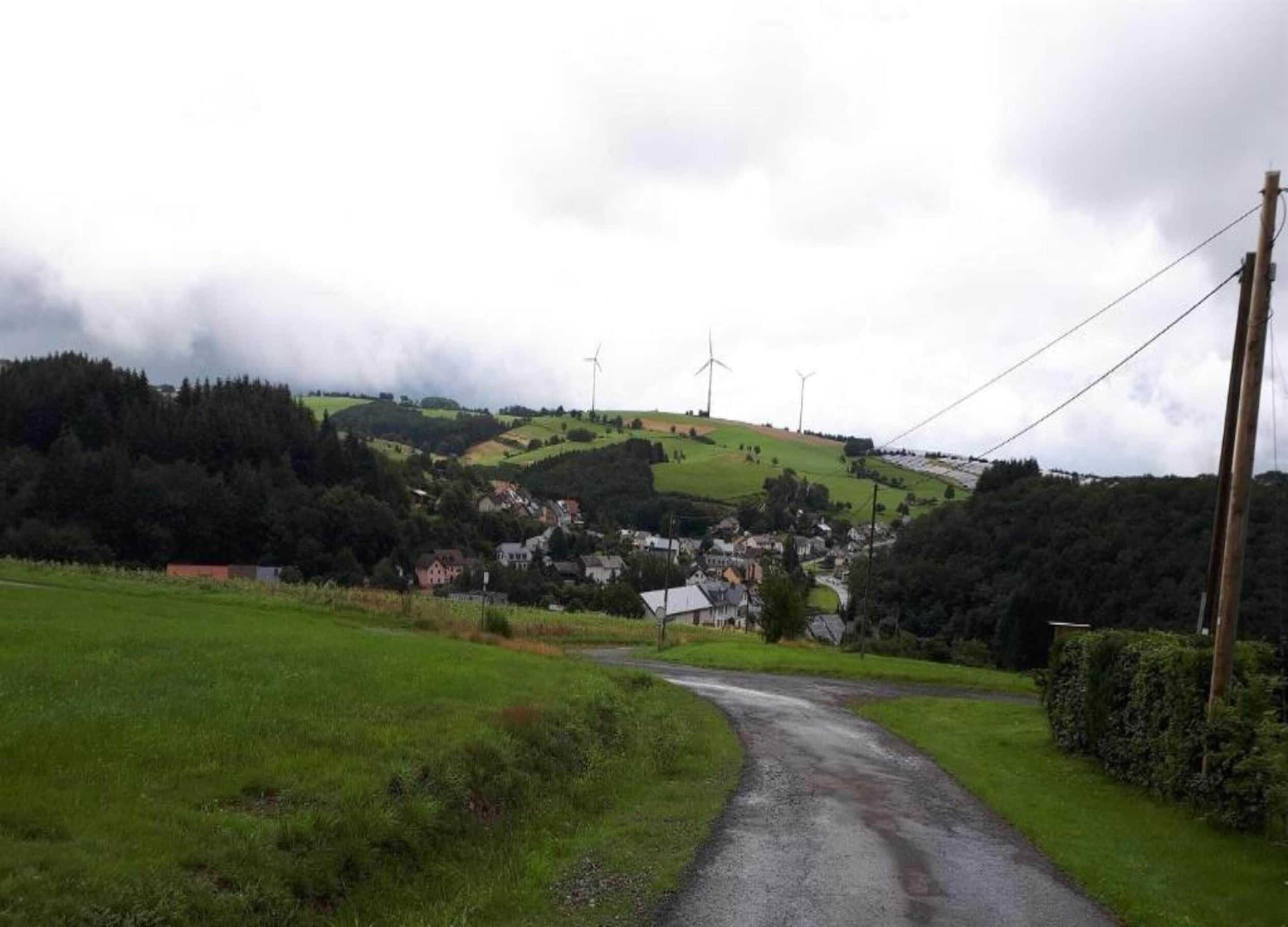 A rural landscape with a winding road leading to a village, surrounded by green fields and hills.