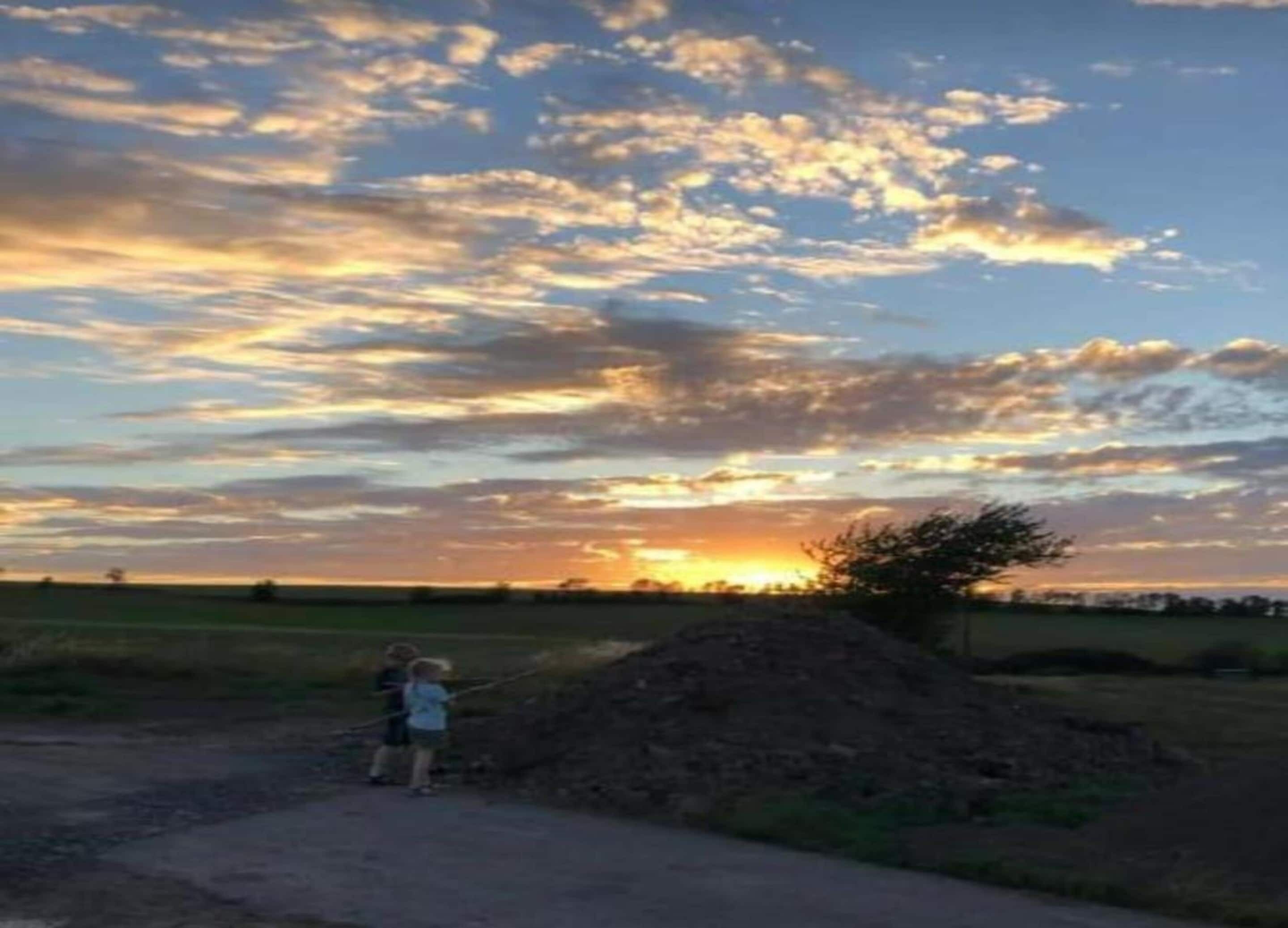 Un coucher de soleil sur un paysage rural, avec un chemin de terre et un tas de terre au premier plan.
