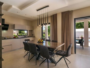 A modern kitchen with a dining area, featuring a large table and chairs, a hanging light fixture, and a view of the outdoors. - Villa Bella Vita (Barban)