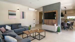 A modern living room with a grey sofa, a coffee table, and a TV mounted on a wooden panel wall. - Villa Bella Vita (Barban)