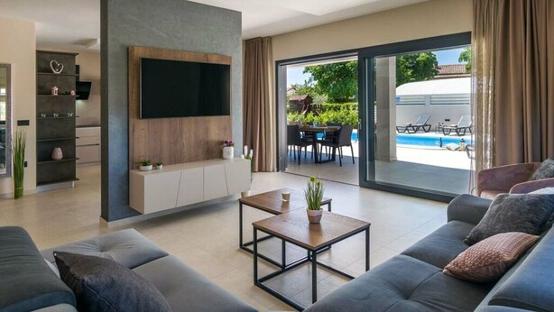 A modern living room with a flat-screen TV, a sofa, a coffee table, and a sliding glass door leading to a pool area. - Villa Bella Vita (Barban)