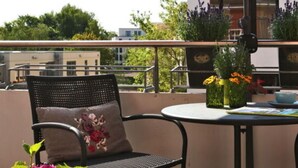 Un balcone con un tavolo rotondo, una sedia con cuscino fiorito e una pianta in vaso con fiori rosa.