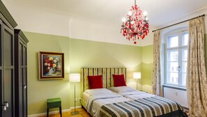 Una camera da letto con un letto, due abat-jour, un piccolo sgabello, un quadro e una finestra con tende.