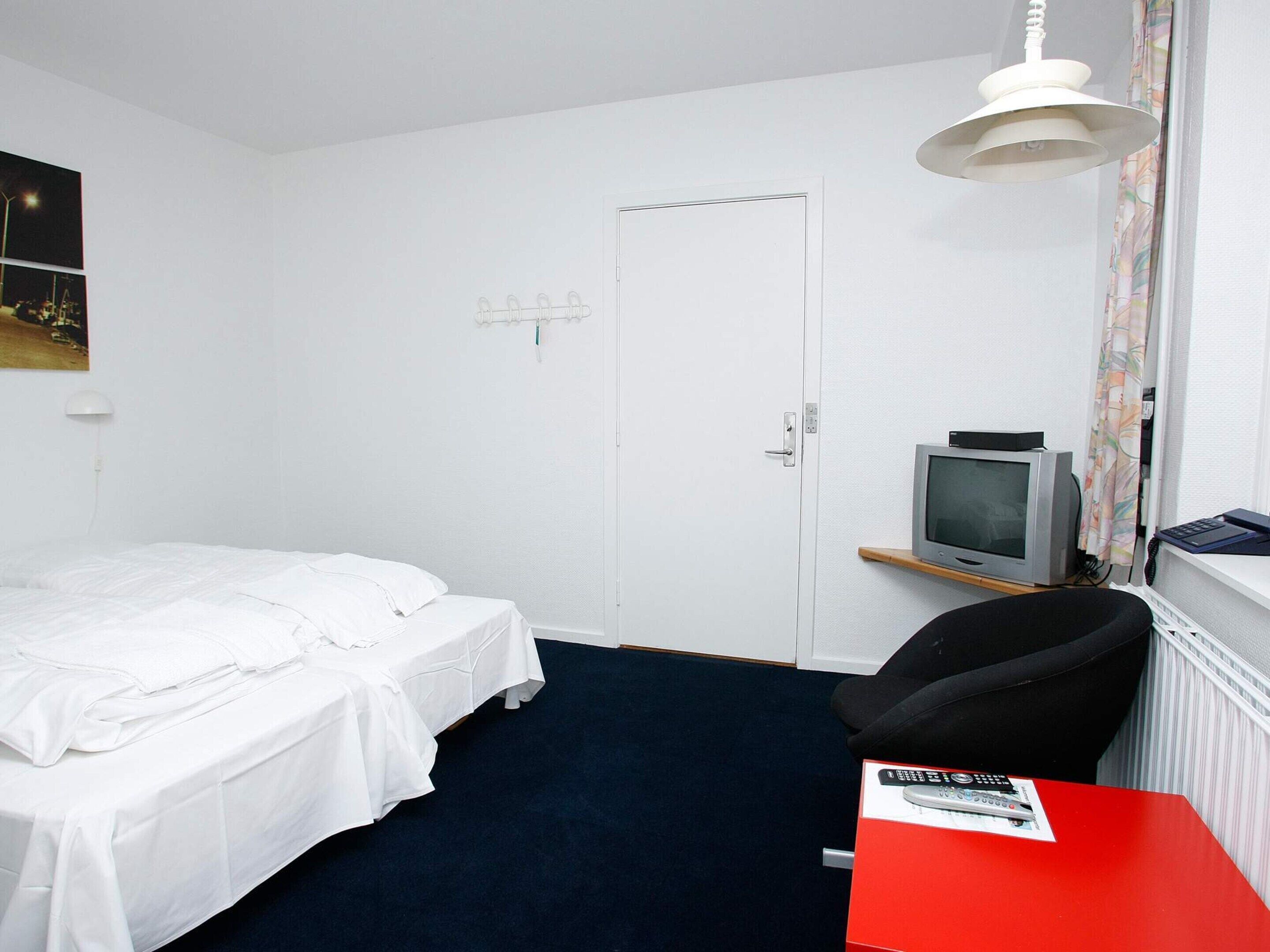 A hotel room with a single bed, a desk with a chair, a television, and a door.