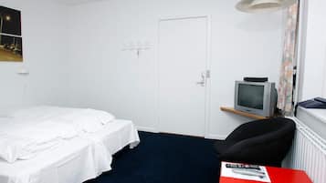 A hotel room with a single bed, a desk with a chair, a television, and a door.