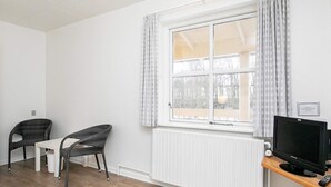 Ein Zimmer mit einem großen Fenster, zwei Korbstühlen, einem kleinen Tisch, einem Fernseher und einer Heizung.