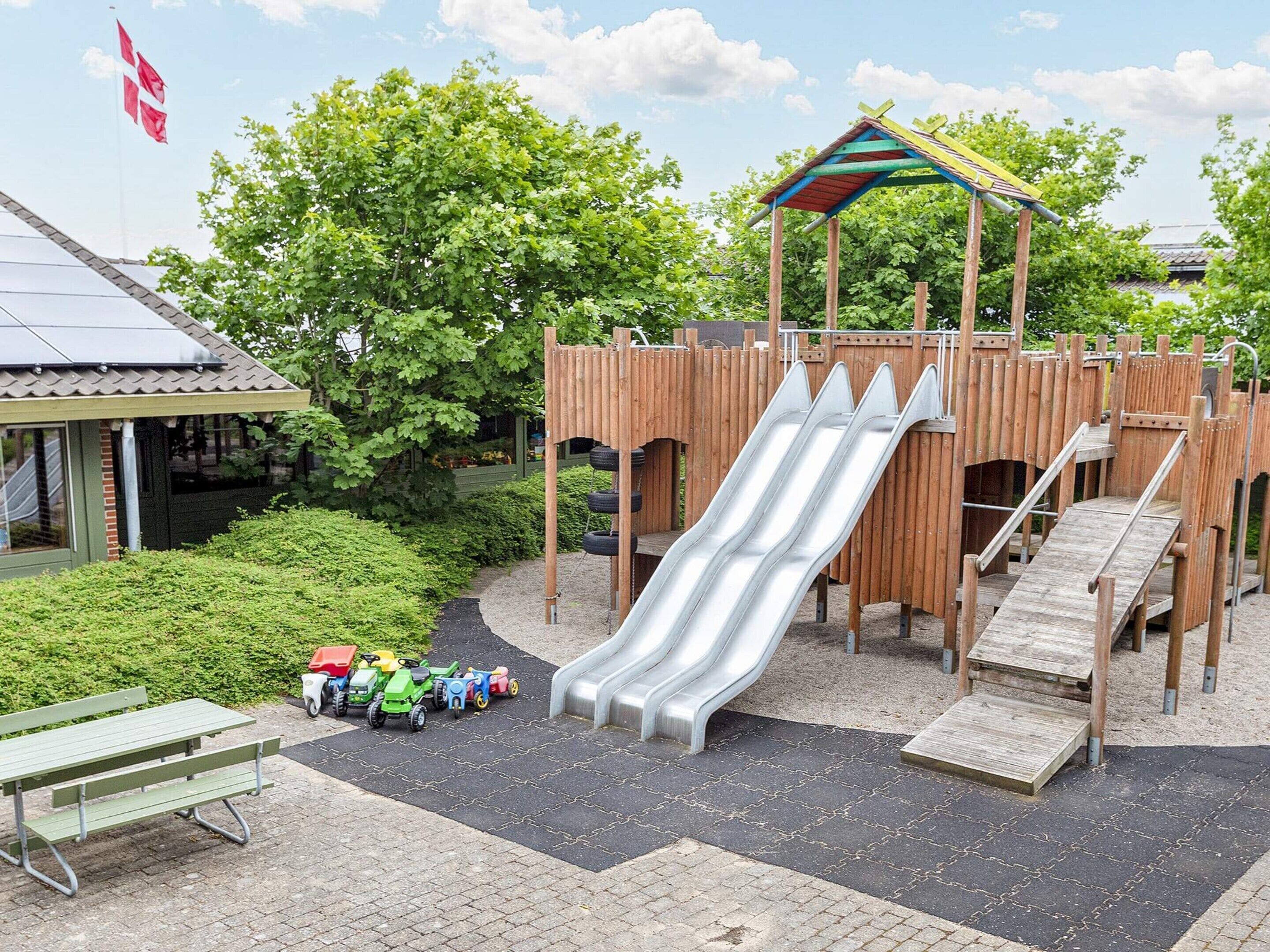 Un parque infantil con tobogán, zona de escalada y una mesa de picnic con vehículos de juguete.