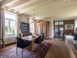 A spacious dining area with a wooden table and chairs, a patterned rug, and a view of the outdoors through large windows. - Premium Farmhouse in Nieuwmunster With Pool (Zuienkerke)