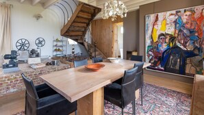 Un comedor con una mesa de madera, sillas negras, una araña y un cuadro abstracto grande, además de una escalera.