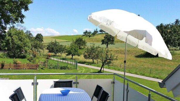 A terrace with a table and chairs, a white umbrella, and a view of a green landscape. - Beech Modern Retreat (Ueberlingen)