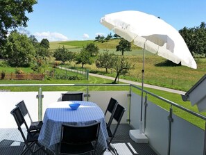 Una terrazza con tavolo e sedie, un ombrellone bianco e vista su un paesaggio verde.