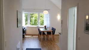 A narrow hallway leading to a dining area with a table and chairs, a blue rug, and a window with a view of trees. - Beech Modern Retreat (Ueberlingen)