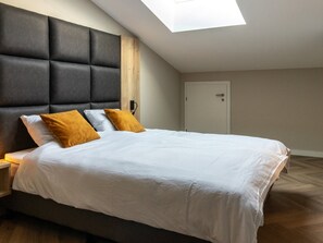 Une chambre moderne avec un grand lit, une tête de lit en bois et une lucarne.