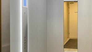 Een liftinterieur met een bedieningspaneel waarop de verdiepingen staan en een blauw bord.