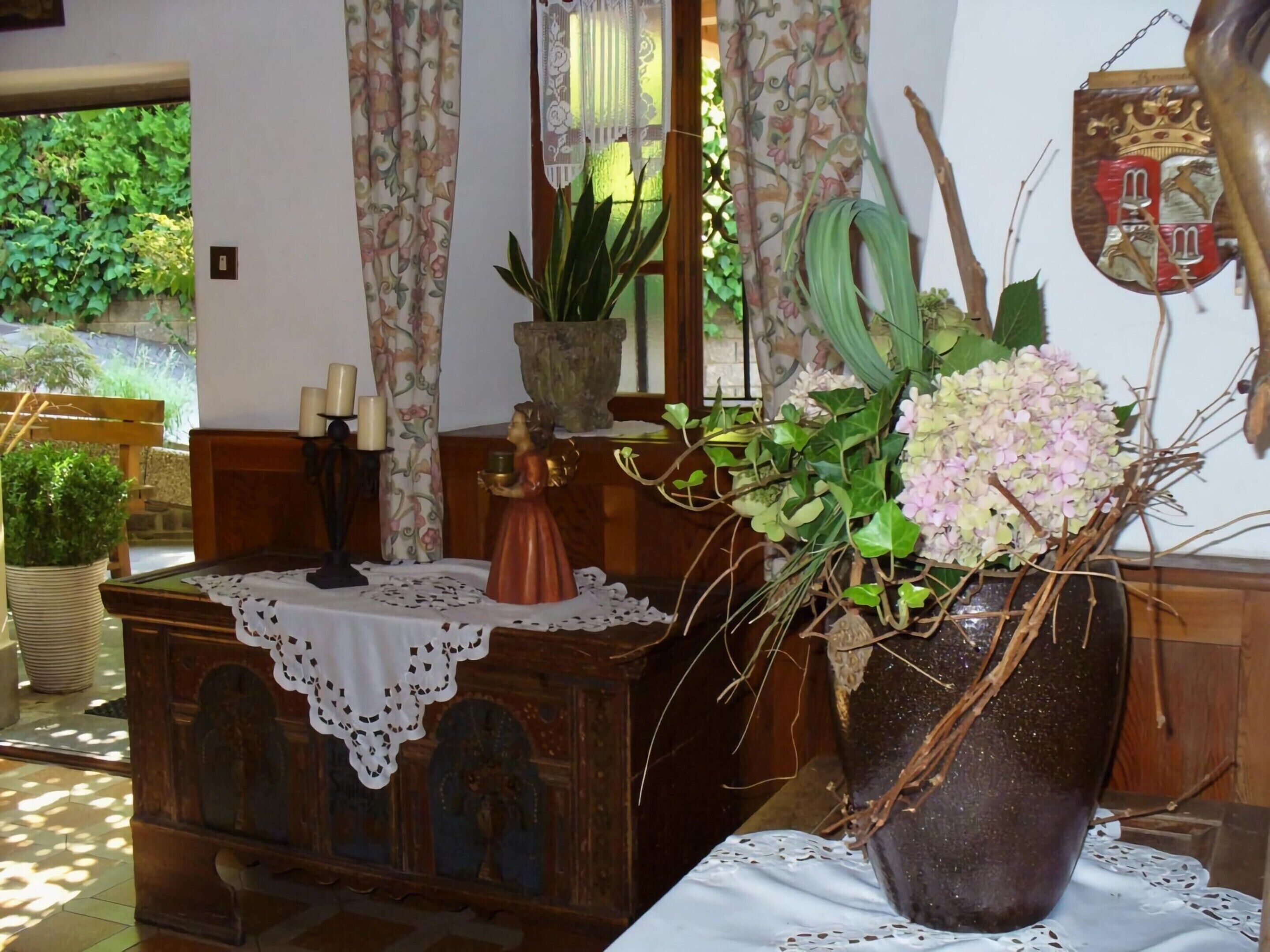 A wooden table with a lace tablecloth, a potted plant, a vase with flowers, and a decorative mirror.