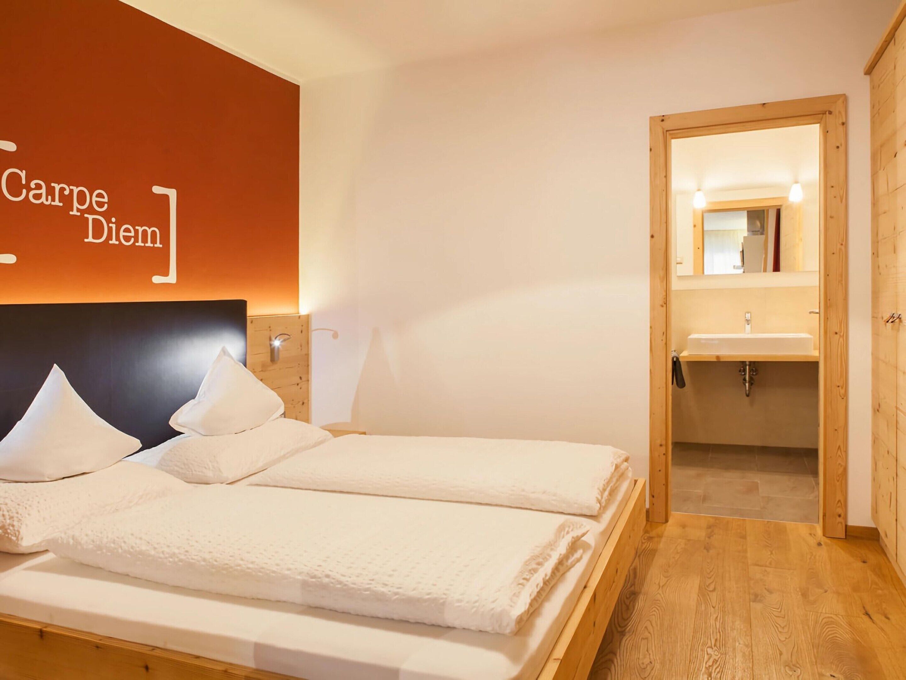 A hotel room with two beds, a wooden headboard, a wall-mounted light, and a wooden door leading to a bathroom with a sink and mirror.