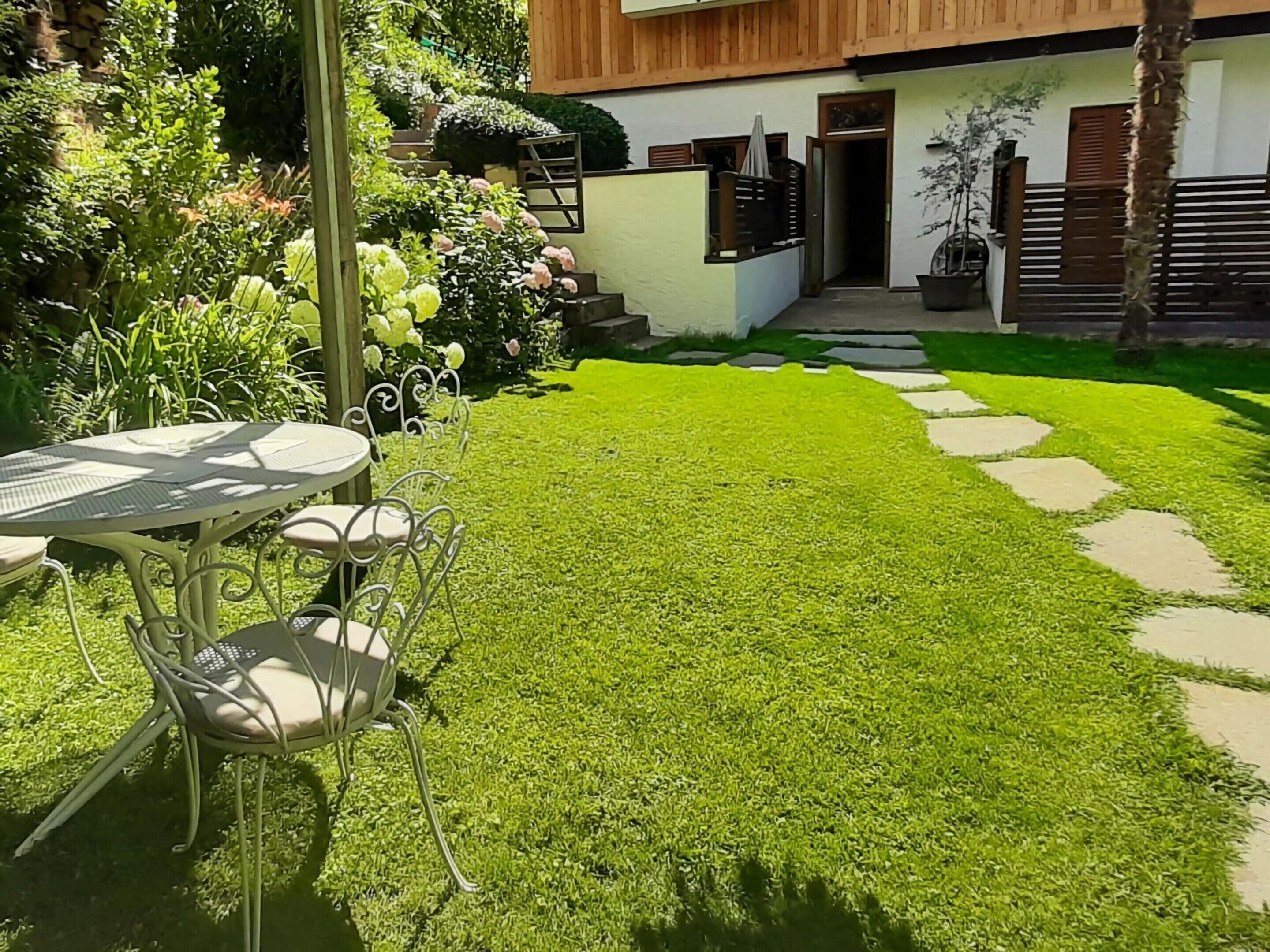 A well-maintained garden with a table and chairs, a stone pathway, and a modern building with a wooden facade.
