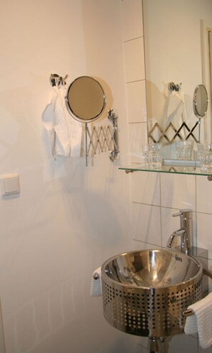 A bathroom with a round mirror, a glass shelf with toiletries, and a stainless steel sink. - App. 2 From Engel & Co (Bad Zwischenahn)