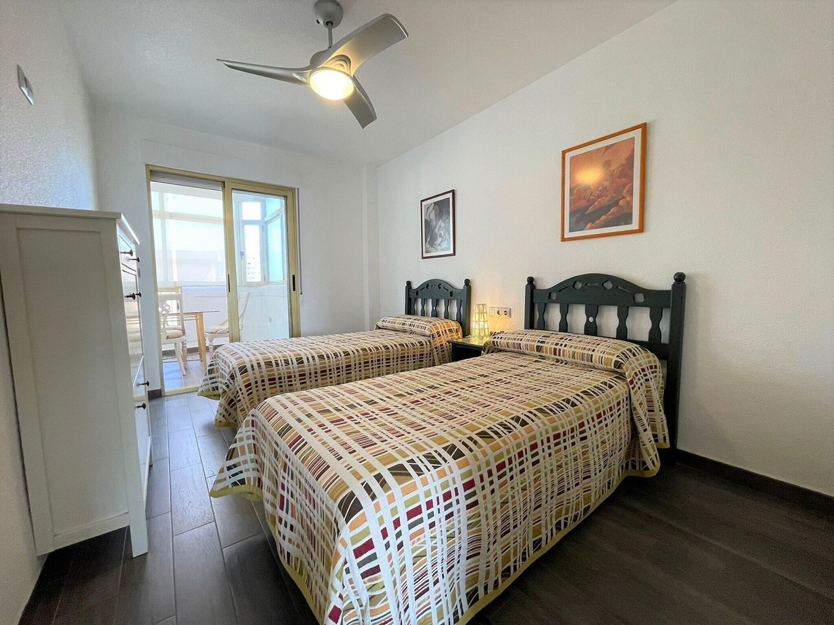 A bedroom with two beds, a ceiling fan, and a painting on the wall.