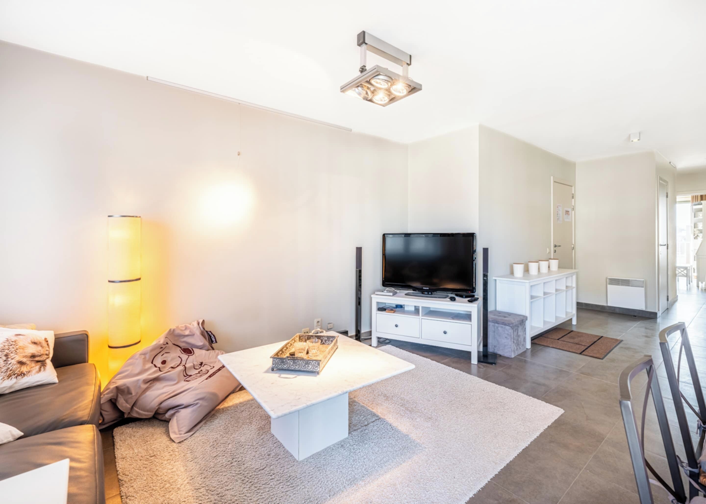 A modern living room with a flat-screen TV, white furniture, and a large floor lamp.