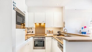 A modern kitchen with white cabinets, stainless steel appliances, and a tiled backsplash. - Apartment by the Coast With Sunny Terrace (Koksijde)