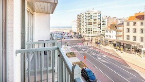A balcony with a view of a city street, a parked car, and buildings in the background. - Apartment by the Coast With Sunny Terrace (Koksijde)