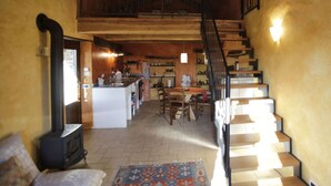 A rustic kitchen with a central island, wooden staircase, and a large window allowing natural light. - Holiday Home Cascina Lovera (Bonvicino)