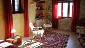 A cozy room with a wooden ceiling, a patterned rug, a wicker chair, a bookshelf, and a window with red curtains. - Holiday Home Cascina Lovera (Bonvicino)