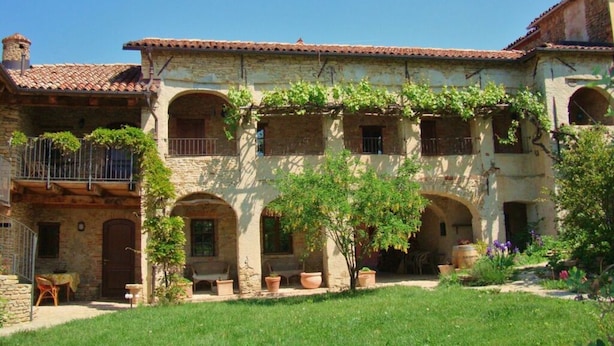 A traditional stone building with arched windows, a covered patio, and a garden with potted plants and flowers. - Holiday Home Cascina Lovera (Bonvicino)
