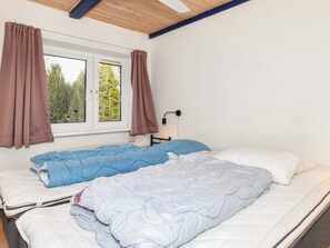 Une chambre avec deux lits, une fenêtre avec des rideaux, une lampe fixée au mur et une vue sur les arbres à l’extérieur.