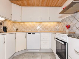 Una cocina con gabinetes blancos, lavavajillas, horno y salpicadero de azulejos.